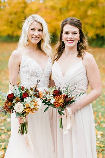 A bride and bridesmaid posing in front of fall colors